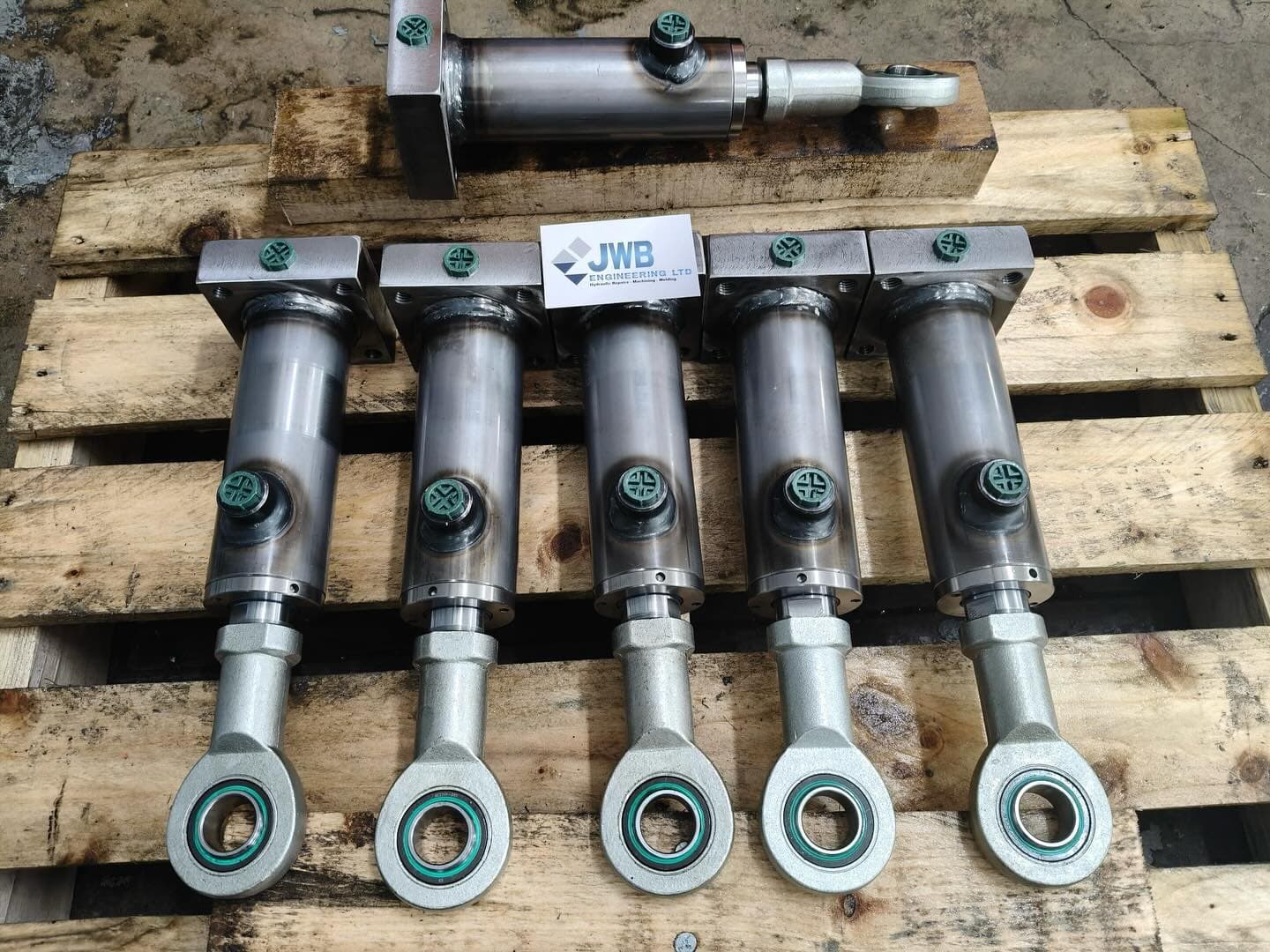 Batch of six rebuilt hydraulic cylinders with rod eye bearings on a pallet at JWB Engineering